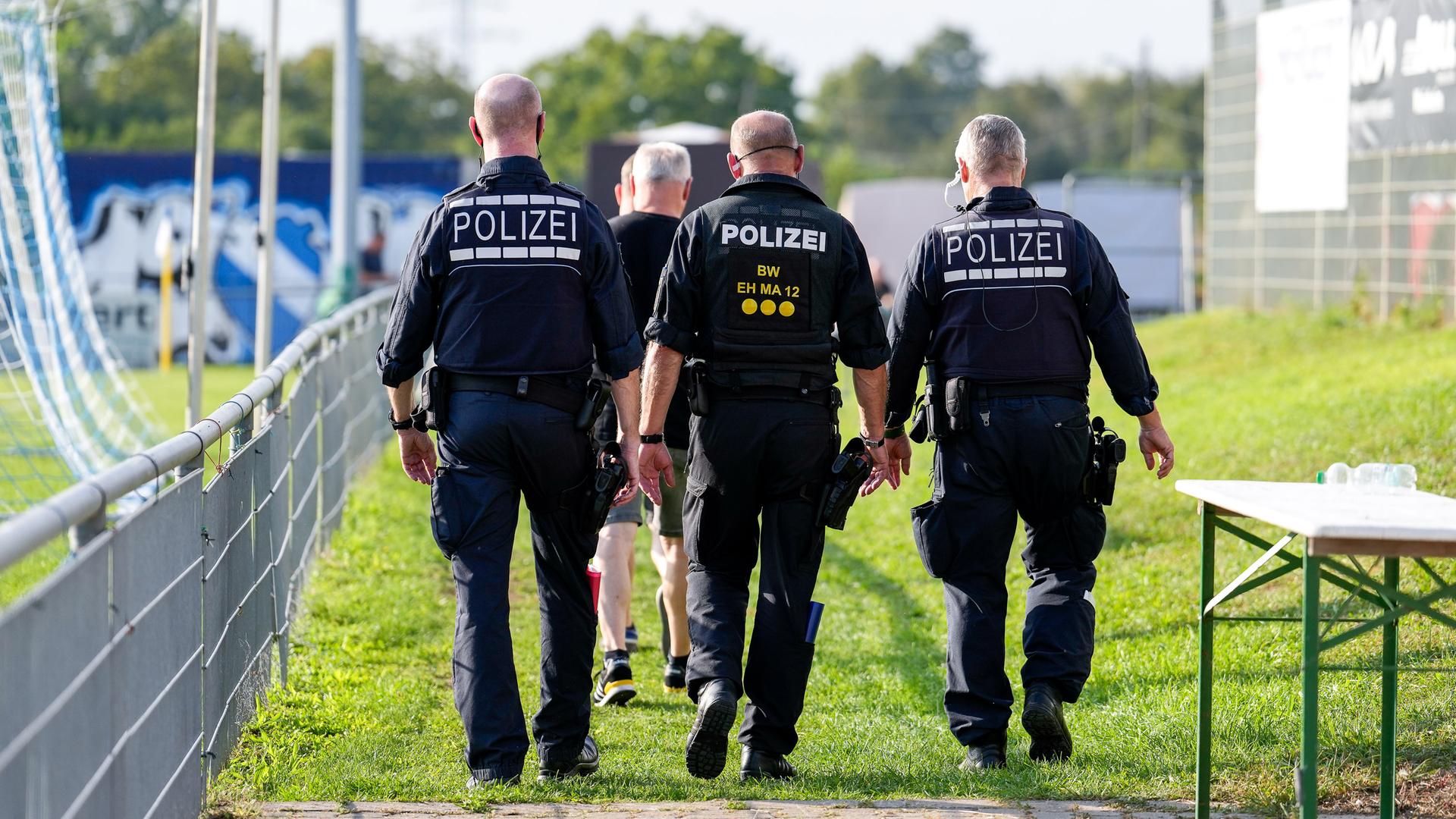 Polizei im Einsatz im Stadion, drei Polizisten laufen auf einem Sportplatz.