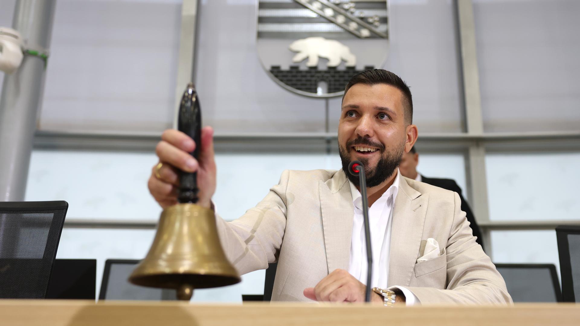 Tobias Rausch läutet im Landtag von Sachsen-Anhalt eine Glocke und lächelt dabei. Tobias Rausch läutet im Landtag von Sachsen-Anhalt eine Glocke und lächelt dabei.