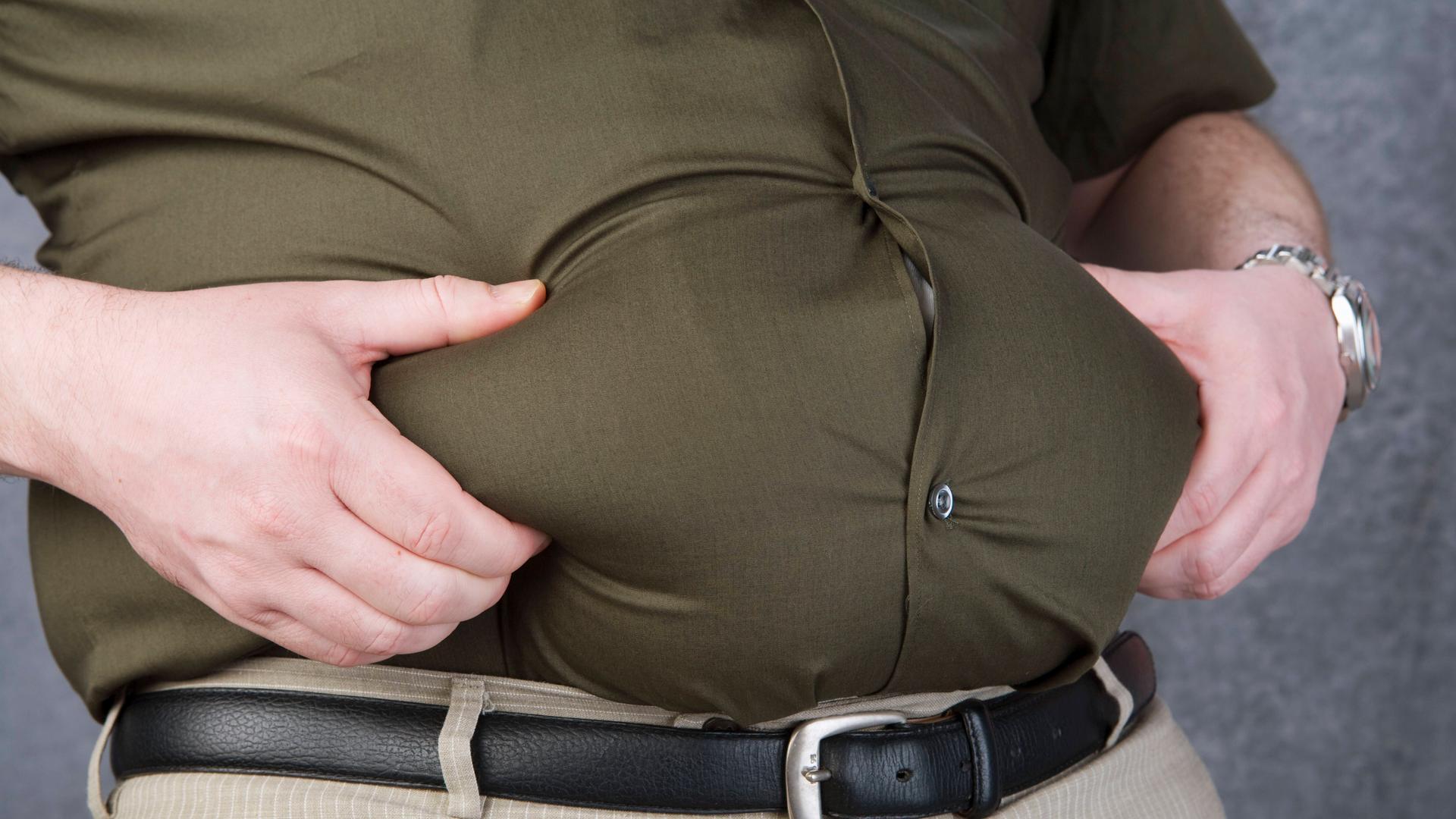 Ein dicker Mann packt in sein Bauchfett.