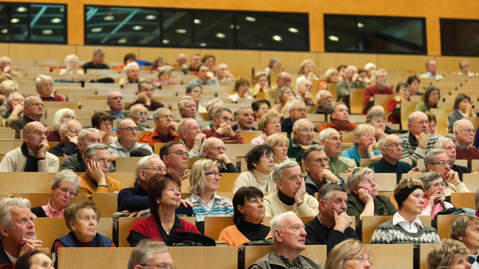 Senioren sitzen bei einer Veranstaltung in den Reihen eines Auditoriums.