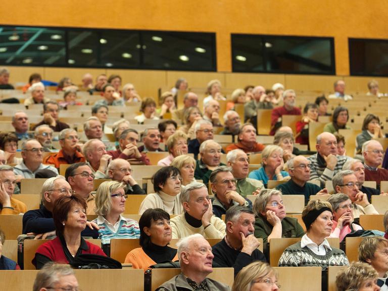 Senioren sitzen bei einer Veranstaltung in den Reihen eines Auditoriums.