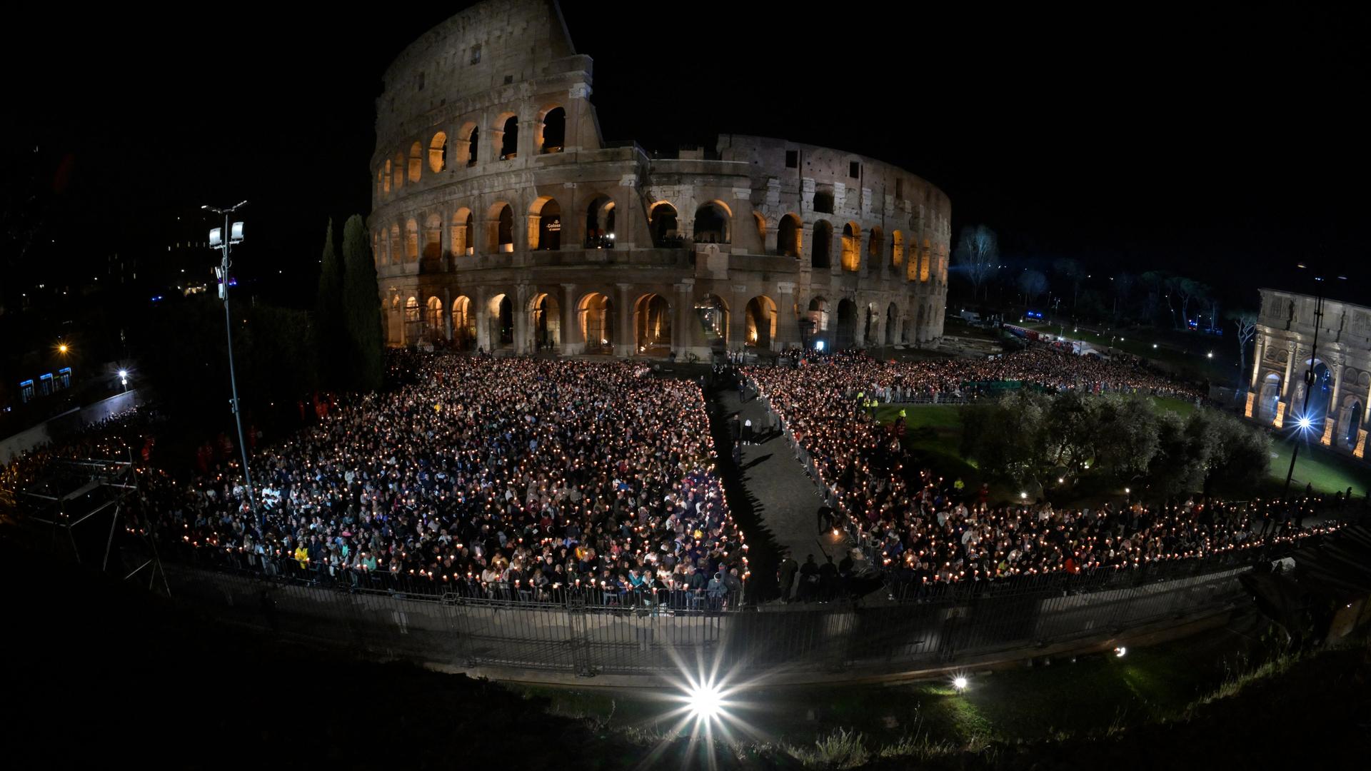 Tausende Menschen haben sich in Rom vor dem erleuchteten Kolosseum versammelt. Viele von ihnen halten Kerzen in der Hand.