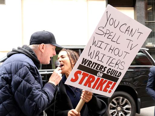 Ein Mann und eine Frau demonstrieten. Die Frau hält ein Plakat hoch, auf dem steht "You can't spell TV without writers" - auf deutsch "Du kannst Fernsehen nicht buchstabieren ohne Drehbuchautoren" 