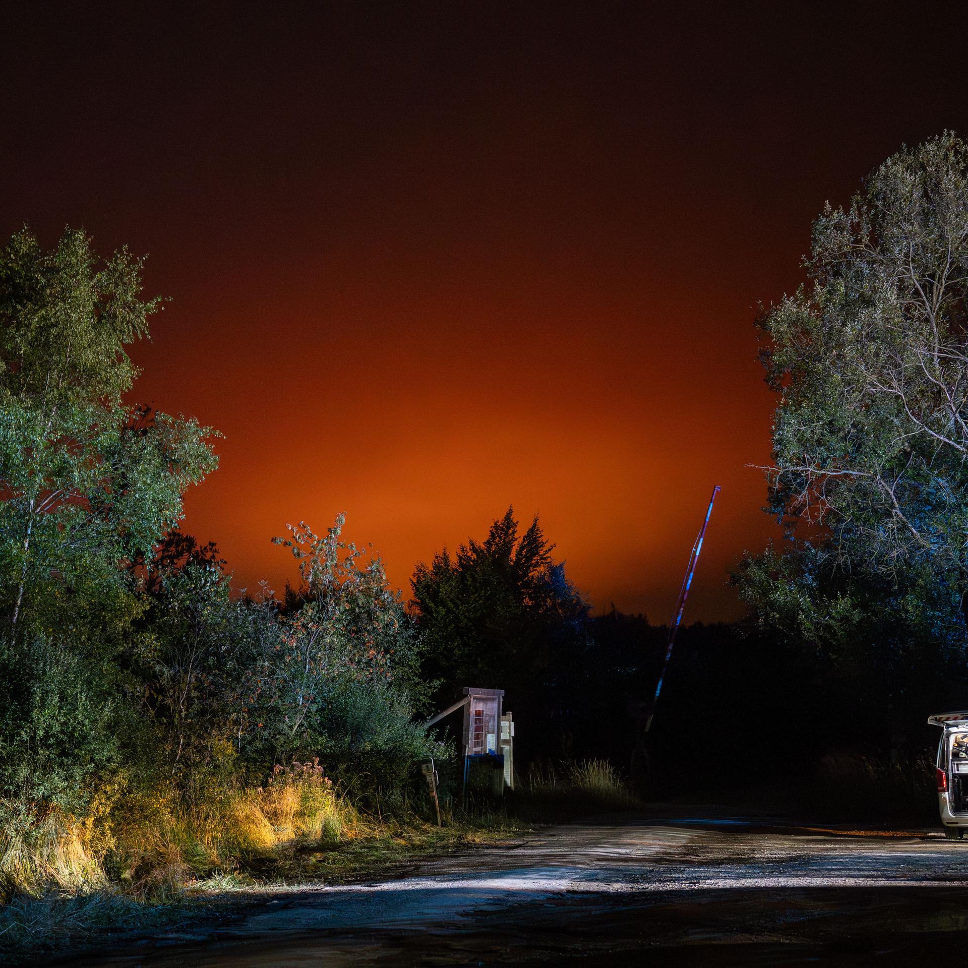 Rettungskräfte stehen auf einem Waldparkplatz. Der Nachthimmel ist rot erhellt vom weiter entfernten Waldbrand. 