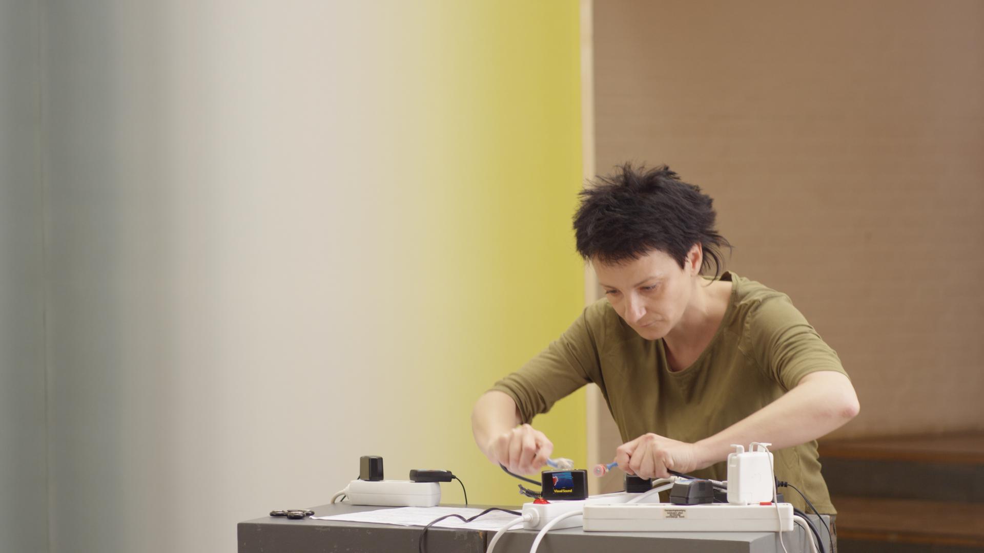 Eine Frau mit kurzen Haaren steht konzentriert an einem Tisch, wobei sie mit Magnetresonanz-Instrumenten hantiert.