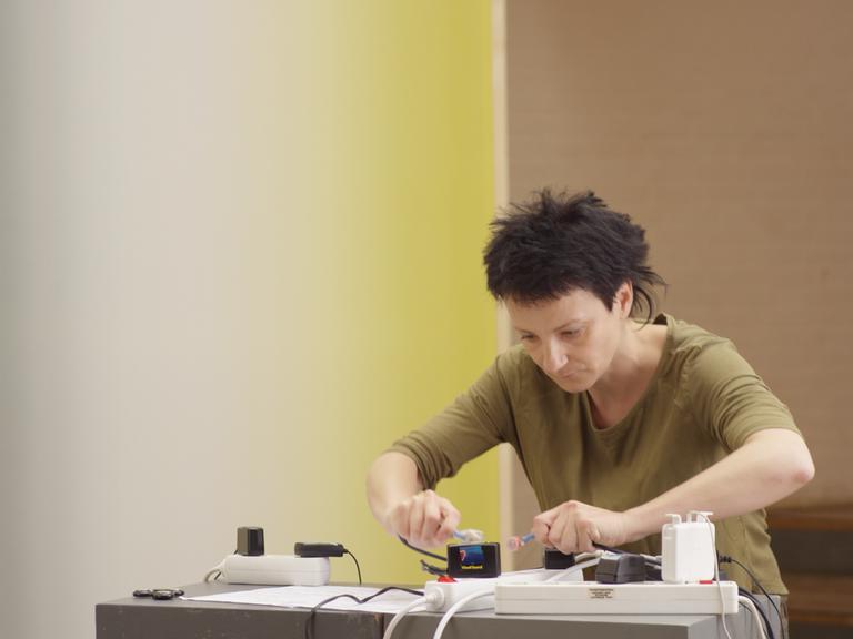Eine Frau mit kurzen Haaren steht konzentriert an einem Tisch, wobei sie mit Magnetresonanz-Instrumenten hantiert.