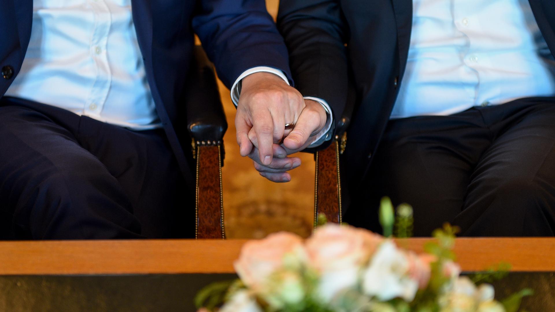 Das Foto zeigt die Hände von zwei Männern, die gerade heiraten.