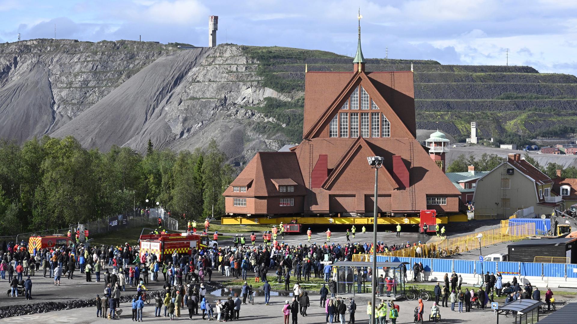 Auf einem speziell konstruierten Wagen mit 224 Rädern wird die Kirche von Kiruna mit einer Geschwindigkeit von einem halben Kilometer pro Stunde bewegt. Viele Menschen schauen zu.