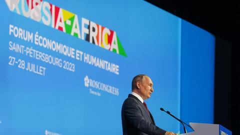 Präsident Putin steht beim Russland-Afrika-Gipfel in Sankt Petersburg auf der Bühne hinter einem Rednerpult. Hinter ihm in bunten Farben das Logo des Gipfels.