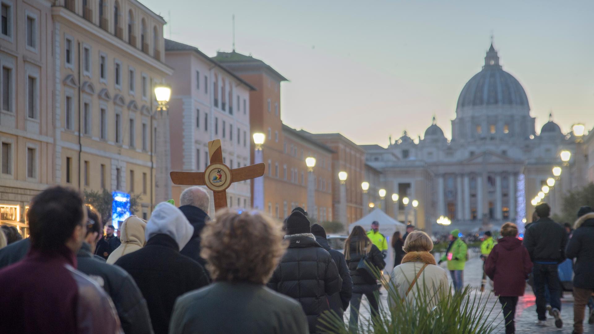 Christliche Pilger laufen mit einem Holzkreuz Ende Dezember 2025 auf den Petersdom zu.