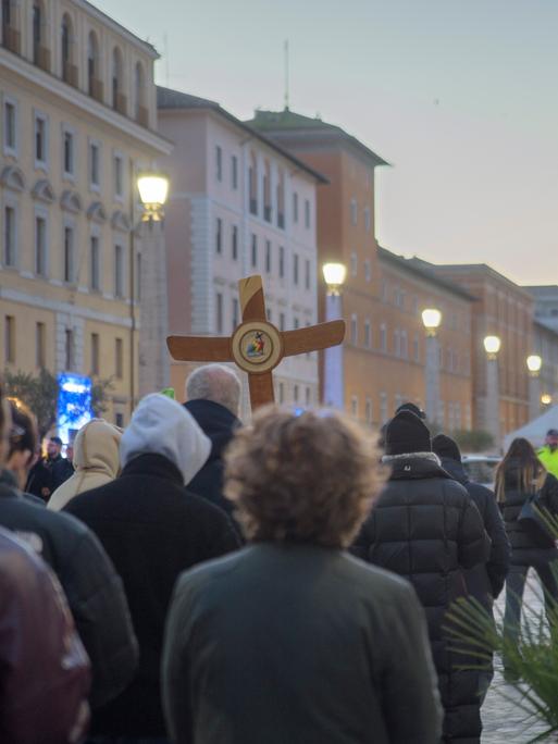 Christliche Pilger laufen mit einem Holzkreuz Ende Dezember 2025 auf den Petersdom zu.