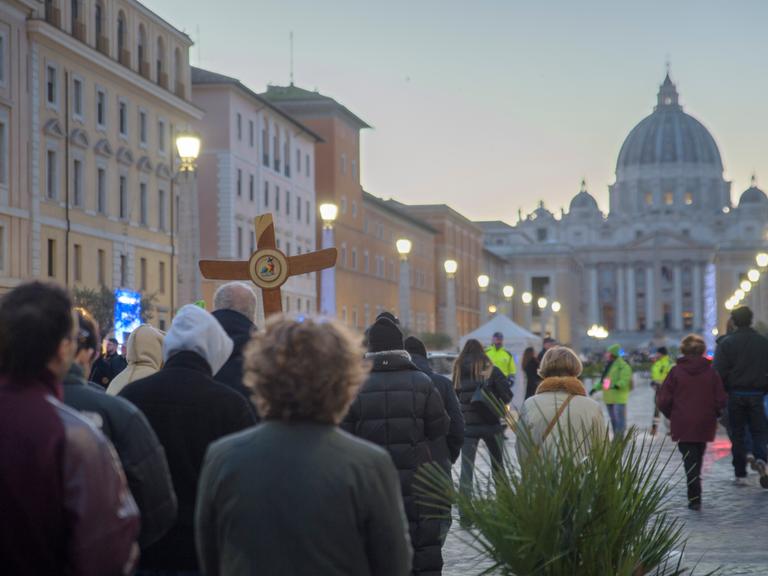 Christliche Pilger laufen mit einem Holzkreuz Ende Dezember 2025 auf den Petersdom zu.