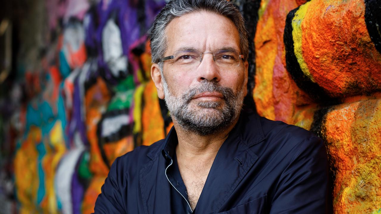 Robert Pfaller steht in dunklem Sakko und verschränkten Armen vor einer farbig besprühten Wand und schaut freundlich in die Kamera.