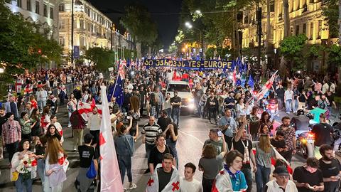 Menschen demonstrieren in Tiflis, Georgien. Eine nächtliche Szene zeigt viele Menschen und Fahnen.
