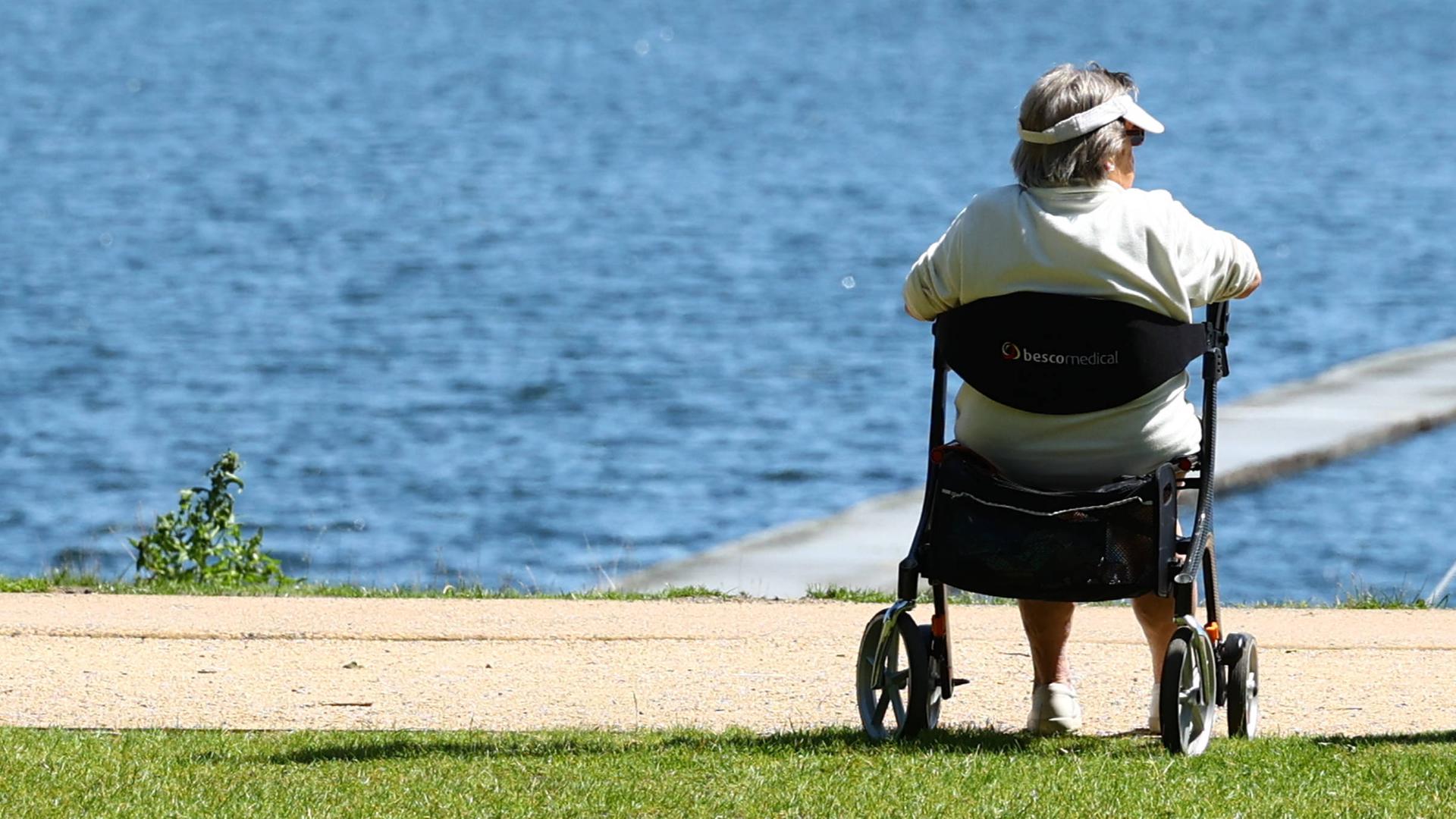 Rentner sitzt auf einem Gehwagen (Rollator) an einem Seeufer in Hamburg Rentner sitzt auf einem Gehwagen (Rollator) an einem Seeufer in Hamburg