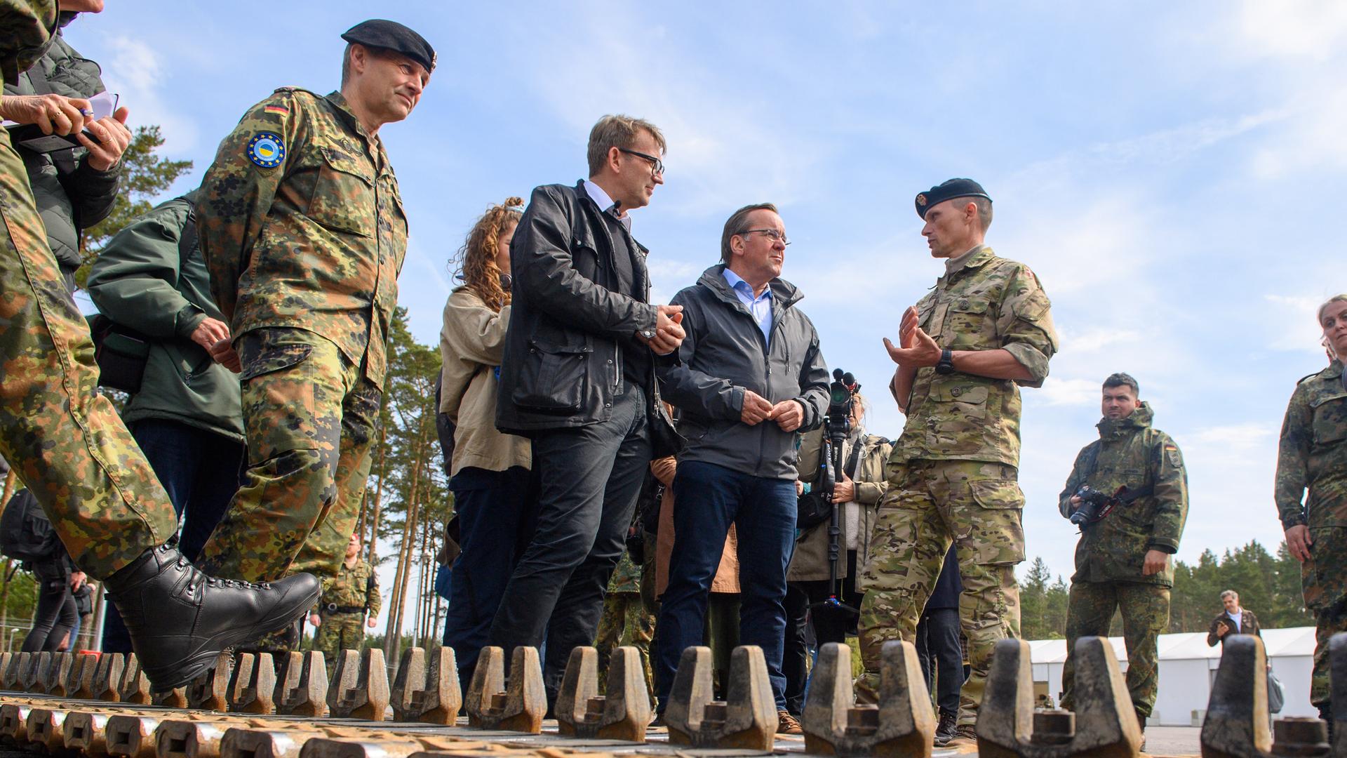Pistorius und Lund Poulsen stehen hinter einer Panzerkette und sprechen mit dem Kommandeur der dänischen Soldaten. Pistorius und Lund Poulsen stehen hinter einer Panzerkette und sprechen mit dem Kommandeur der dänischen Soldaten.