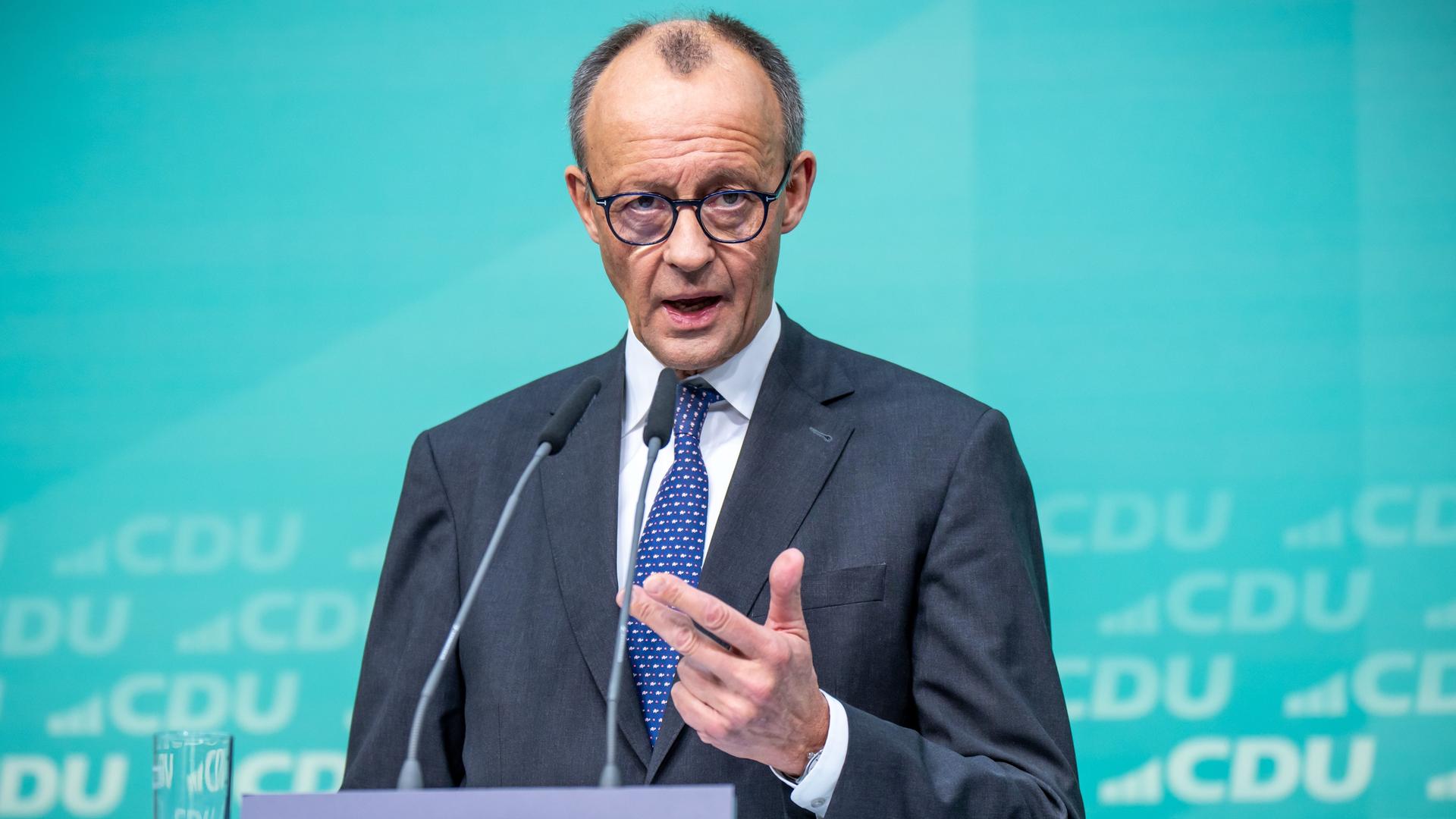 Friedrich Merz spricht bei der Pressekonferenz an einem Rednerpult. Er trägt Anzug mit Krawatte und eine runde Brille.