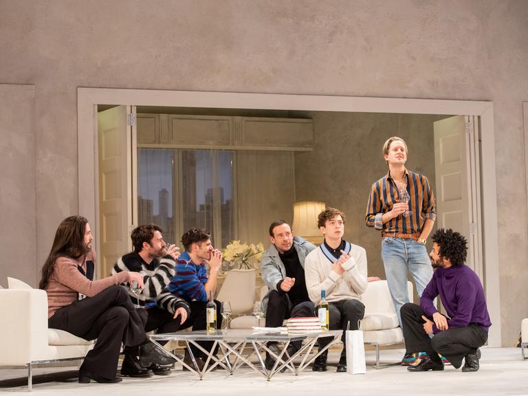 Foto von der Inszenierung: Sieben junge Männer unterhalten sich angeregt auf einer Couch-Landschaft miteinander.