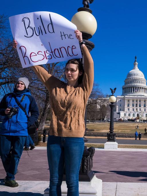 Drei Menschen, mit Flagge und einem bemalten Schild protestieren gegen Trump vor dem Kapitolgebäude in Washington