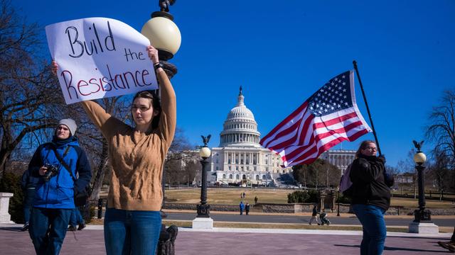 Drei Menschen, mit Flagge und einem bemalten Schild protestieren gegen Trump vor dem Kapitolgebäude in Washington