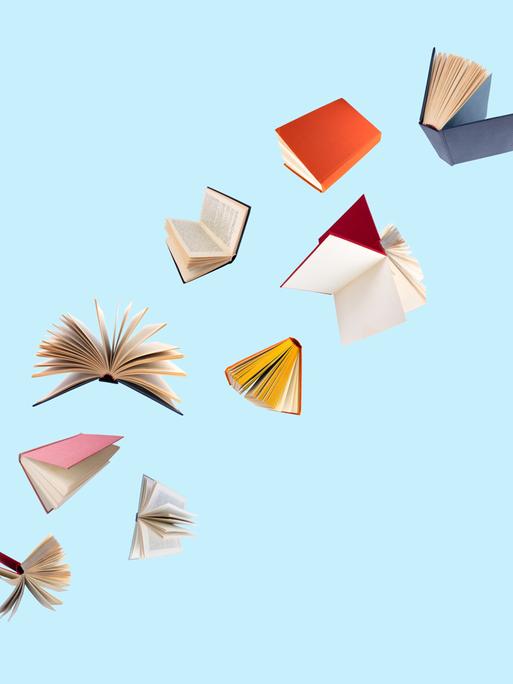 Farbenfroh bezogene Bücher fliegen vor einem blauen Hintergrund durch die Luft