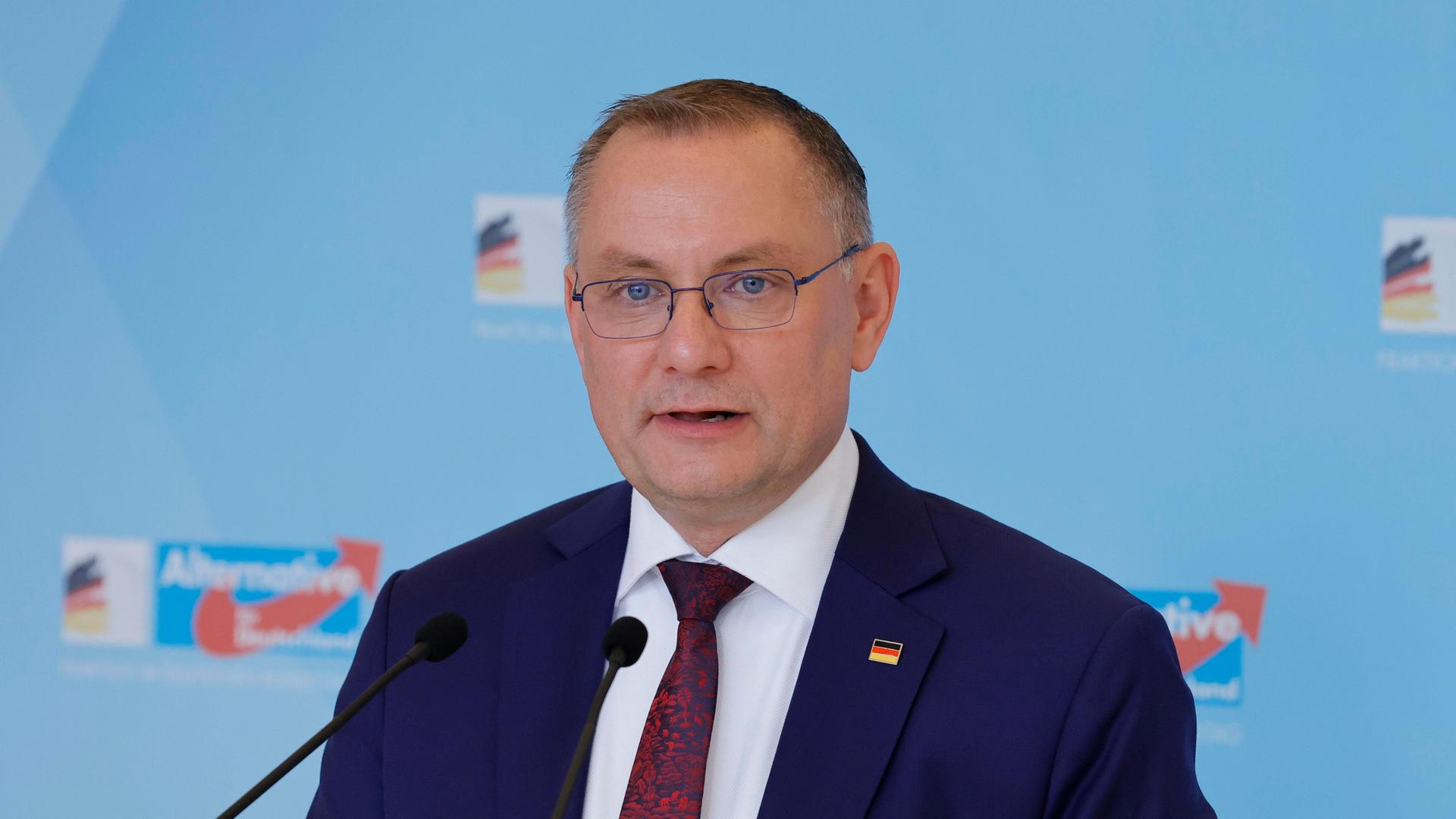Der AfD-Politiker Tino Chrupalla steht an einem Rednerpult, hinter ihm eine blaue Wand mit der Aufschrift "Alternative für Deutschland" Der AfD-Politiker Tino Chrupalla steht an einem Rednerpult, hinter ihm eine blaue Wand mit der Aufschrift "Alternative für Deutschland"