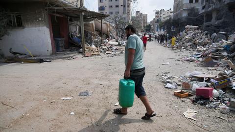 Ein Mann trägt einen Wasserkanister entlang einer zerstörten Straße