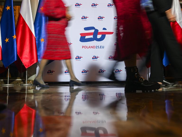 Menschen gehen vor einem Transparent mit der Aufschrift "EU Poland25.EU" vorbei - Beginn der EU-Ratspräsidentschaft von Polen Anfang Januar 2025