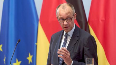  Bundeskanzler Friedrich Merz (CDU) spricht bei einer Pressekonferenz zwei deutschen Fahnen und einer EU-Flagge.