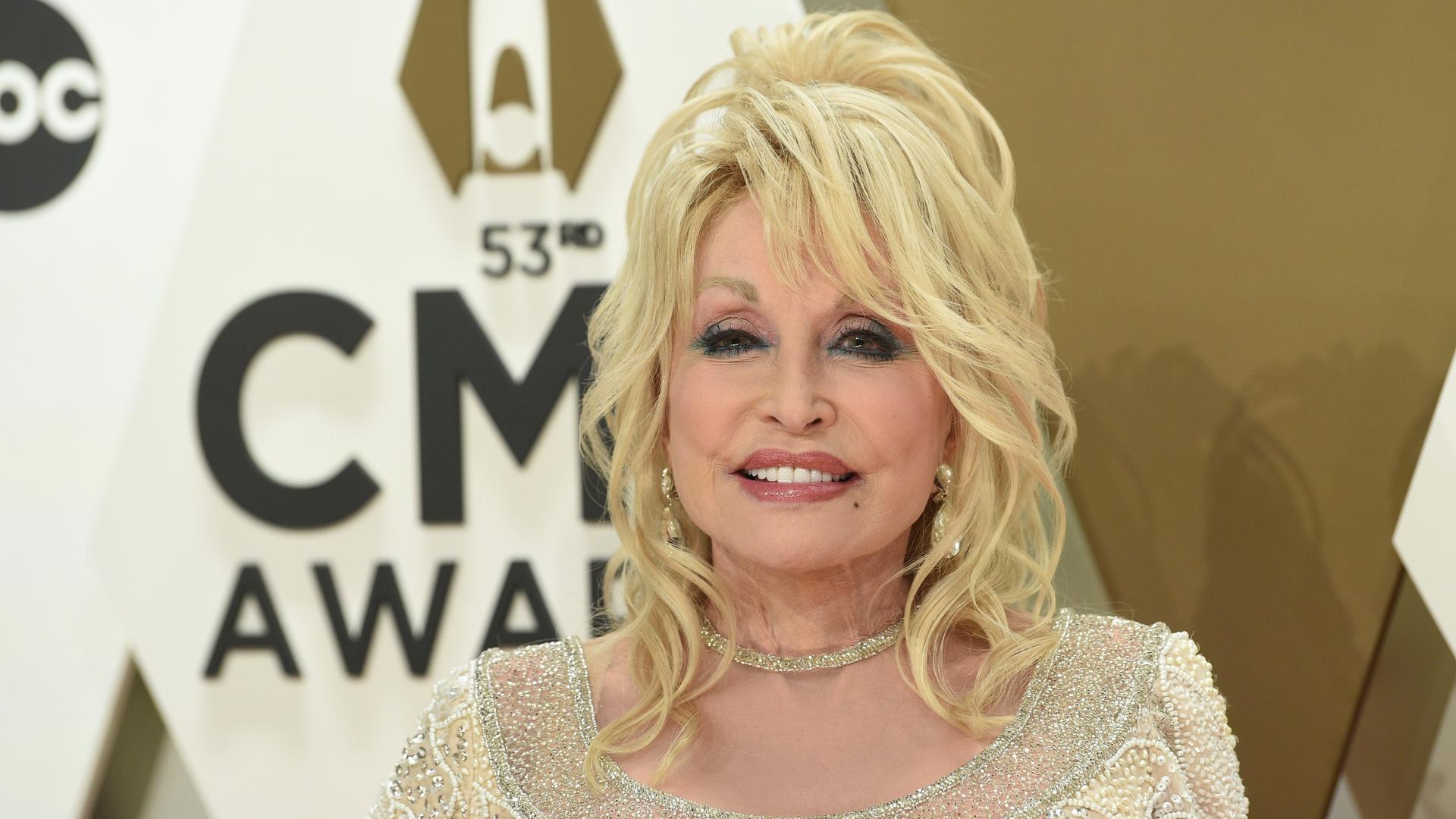 Dolly Parton am 13. November 2019, sie trägt ein gold-glitzerndes Oberteil und lächelt in die Kamera.
