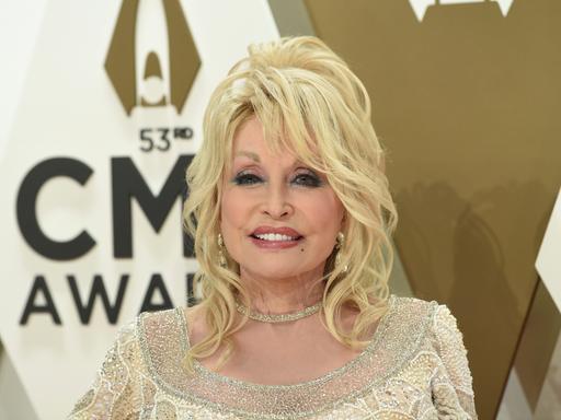 Dolly Parton am 13. November 2019, sie trägt ein gold-glitzerndes Oberteil und lächelt in die Kamera.