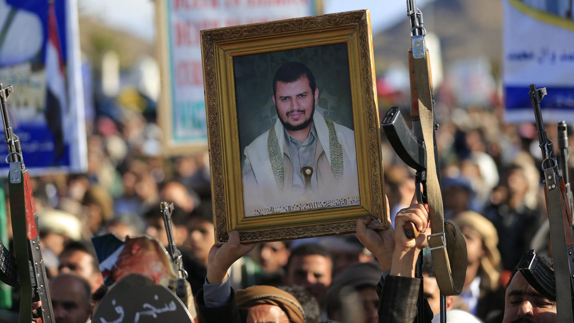 Huthi-Unterstützer auf einer Demonstration. Einige halten Schilder mit Fotos hoch, andere ihre Gewehre. 