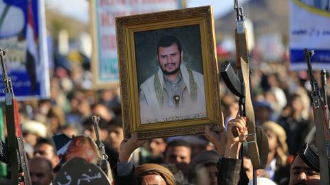 Huthi-Unterstützer auf einer Demonstration. Einige halten Schilder mit Fotos hoch, andere ihre Gewehre. 