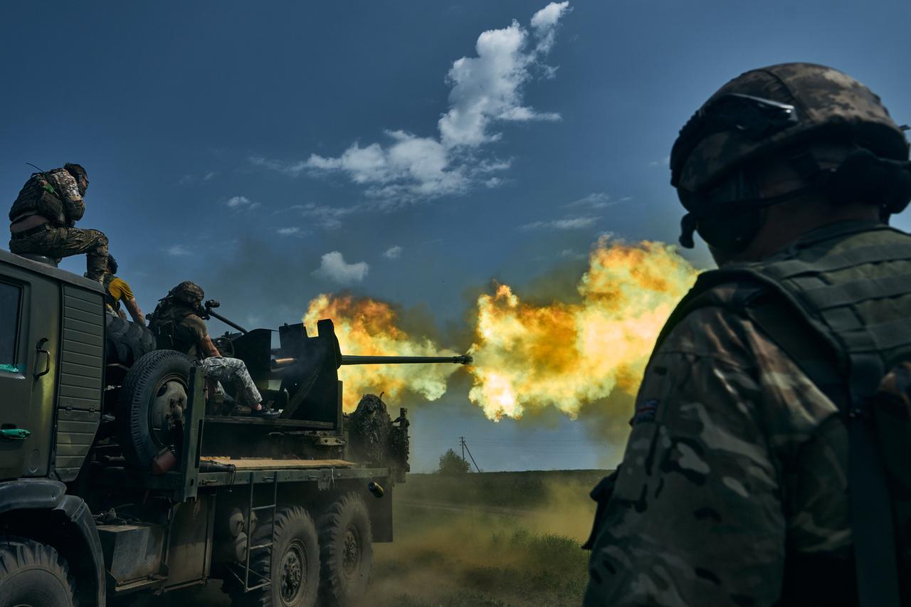 Drei ukrainische Soldaten feuern eine Kanone ab und betrachten das Mündungsfeuer