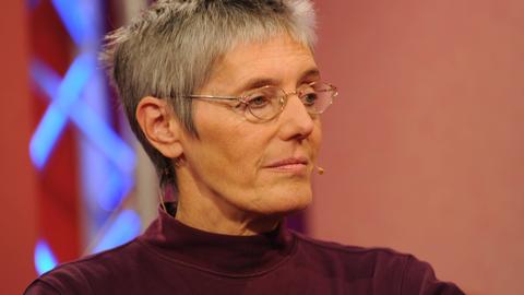Petra Morsbach sitzt in einem Fernsehstudio und schaut zur Seite. Sie hat kurze Haare und trägt eine Brille.