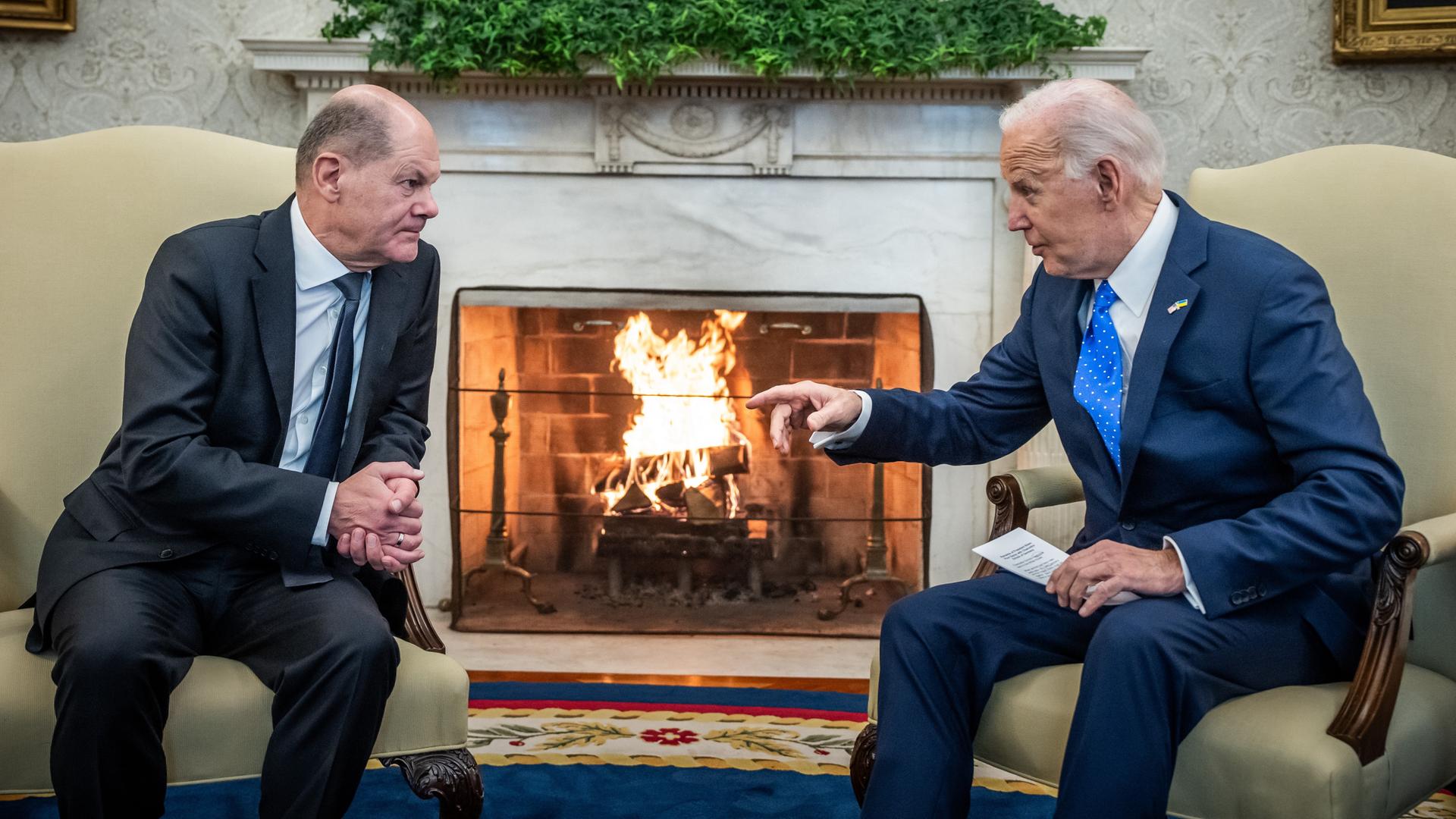 Bundeskanzler Scholz und US-Präsident Biden sitzen sich in Sesseln gegenüber und unterhalten sich. Biden gestikuliert mit der rechten Hand. Im Hintergrund lodert ein Kaminfeuer.