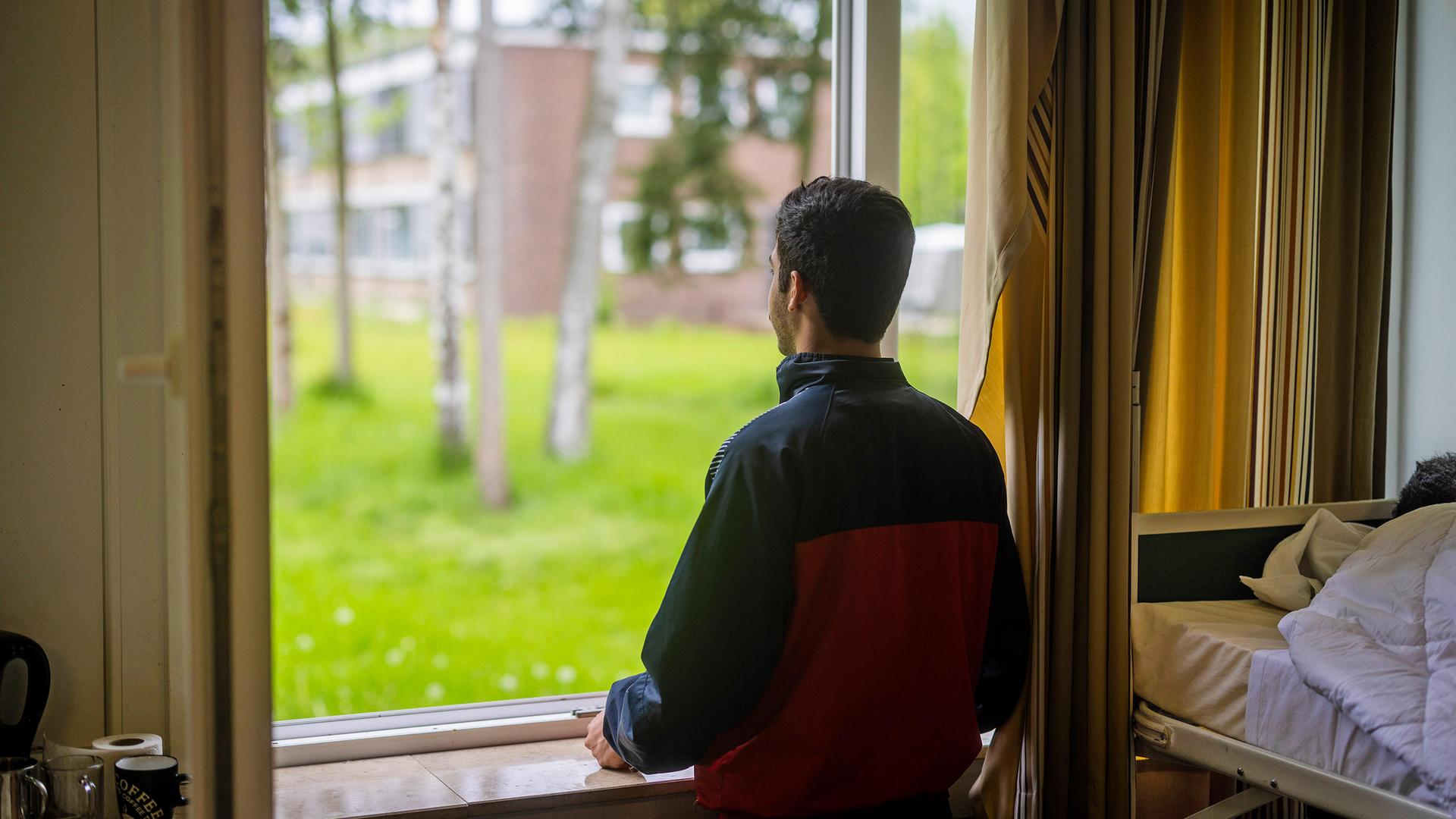 Ein junger Mann aus Syrien blickt aus dem Fenster seiner Unterkunft in der Erstaufnahmeeinrichtung fuer Geflüchtete in Bramsche-Hesepe in Niedersachen bei Osnabrück.