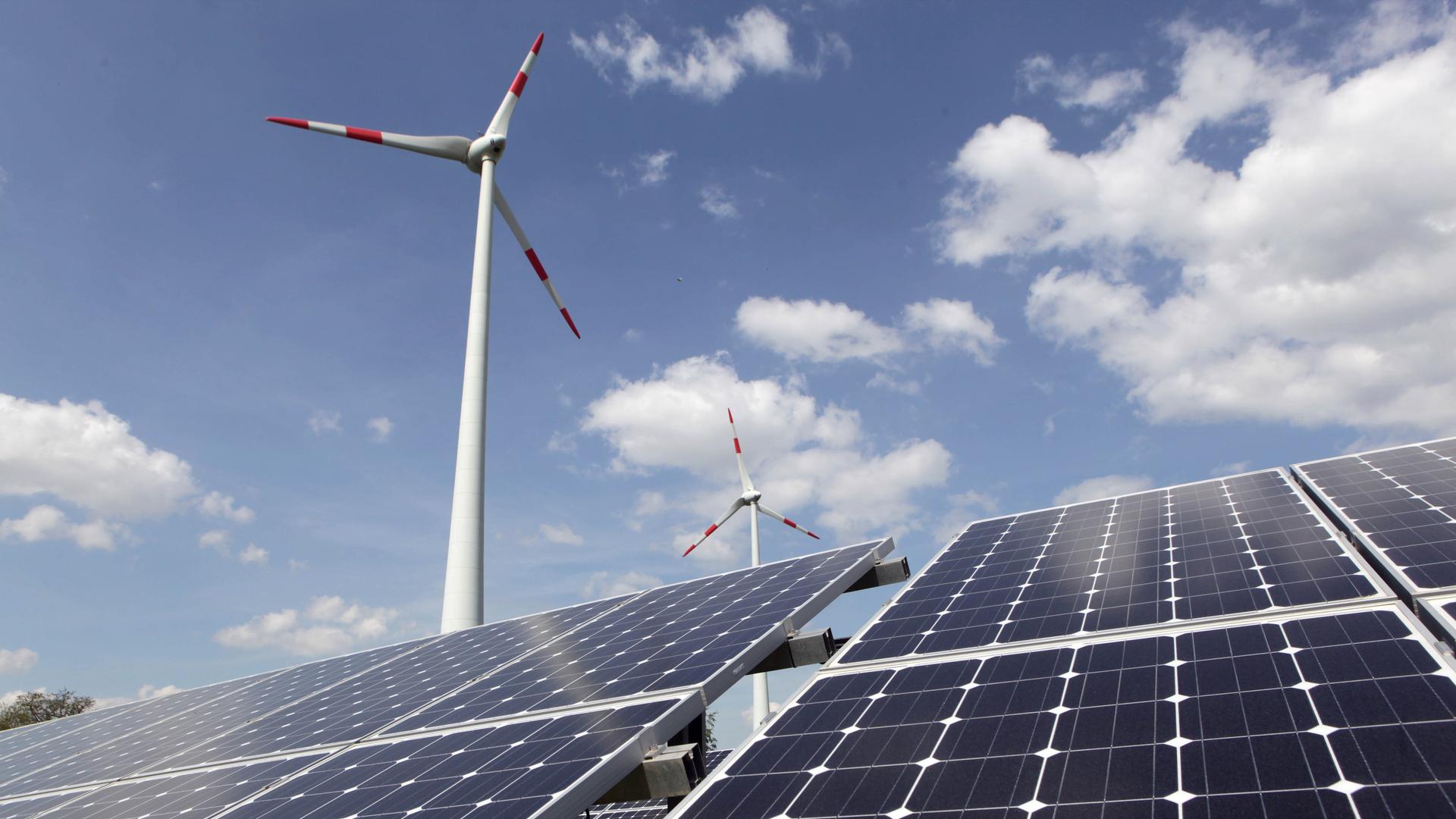 Solarpanels stehen vor zwei Windkraftanlagen.