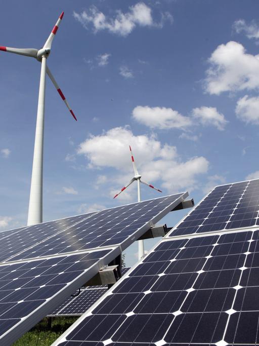 Solarpanels stehen vor zwei Windkraftanlagen.