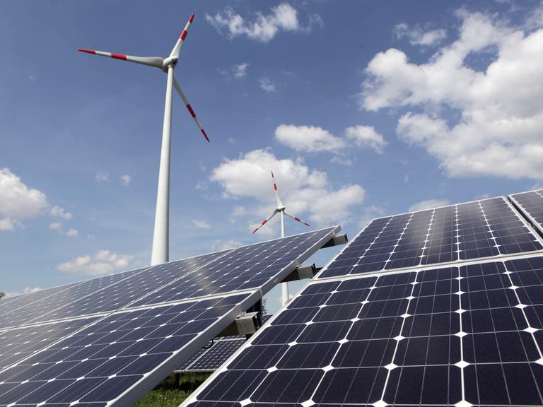 Solarpanels stehen vor zwei Windkraftanlagen.