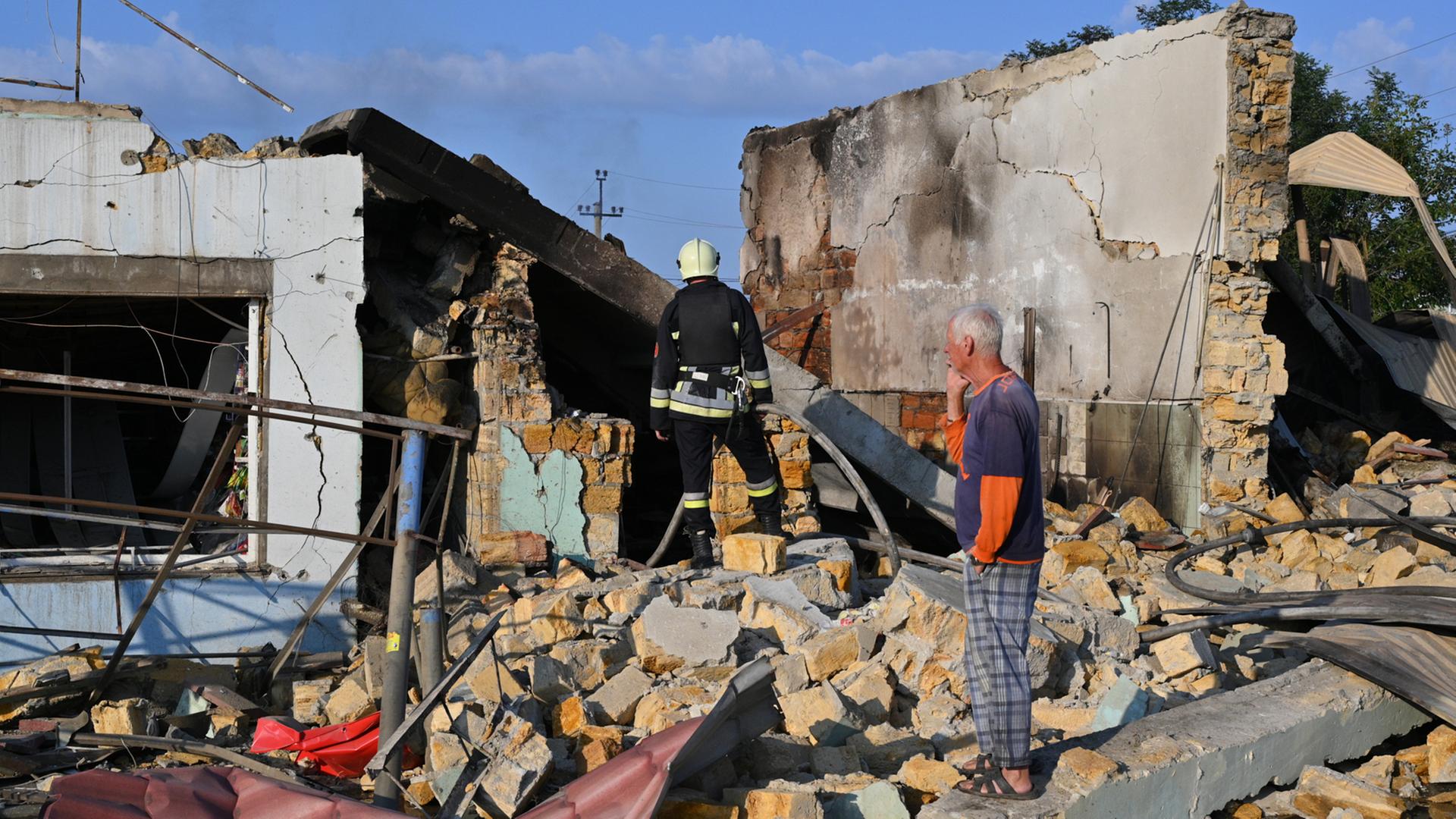 Ein Anwohner betrachtet die Zerstörungen nach einem russischen Raketenangriff. Er steht in den Trümmern eines Hauses. Im Hintergrund steht ein Feuerwehrmann. Ein Anwohner betrachtet die Zerstörungen nach einem russischen Raketenangriff. Er steht in den Trümmern eines Hauses. Im Hintergrund steht ein Feuerwehrmann.