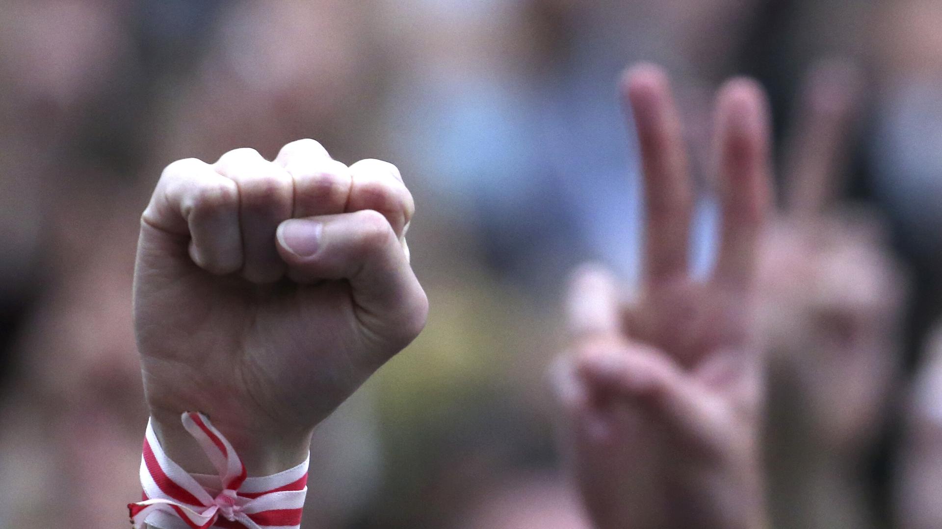 Ein Mensch streckt während einer Oppositionskundgebung im Jahr 2020 auf dem Unabhängigkeitsplatz in Minsk seine Faust in die Höhe. Er trägt ein weiß-rotes Armband, es sind die Farben der Opposition. Ein Mensch streckt während einer Oppositionskundgebung im Jahr 2020 auf dem Unabhängigkeitsplatz in Minsk seine Faust in die Höhe. Er trägt ein weiß-rotes Armband, es sind die Farben der Opposition.