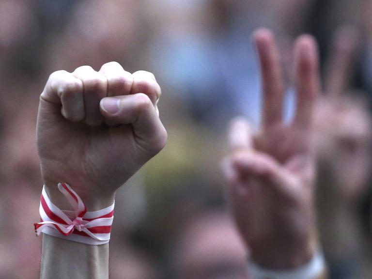 Ein Mensch streckt während einer Oppositionskundgebung im Jahr 2020 auf dem Unabhängigkeitsplatz in Minsk seine Faust in die Höhe. Er trägt ein weiß-rotes Armband, es sind die Farben der Opposition. Ein Mensch streckt während einer Oppositionskundgebung im Jahr 2020 auf dem Unabhängigkeitsplatz in Minsk seine Faust in die Höhe. Er trägt ein weiß-rotes Armband, es sind die Farben der Opposition.