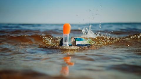 Blick vom Strand aufs Wasser. Ein kind nähert sich, mit Taucherbrille und Schnorchel, das Gesicht unter Wasser.
