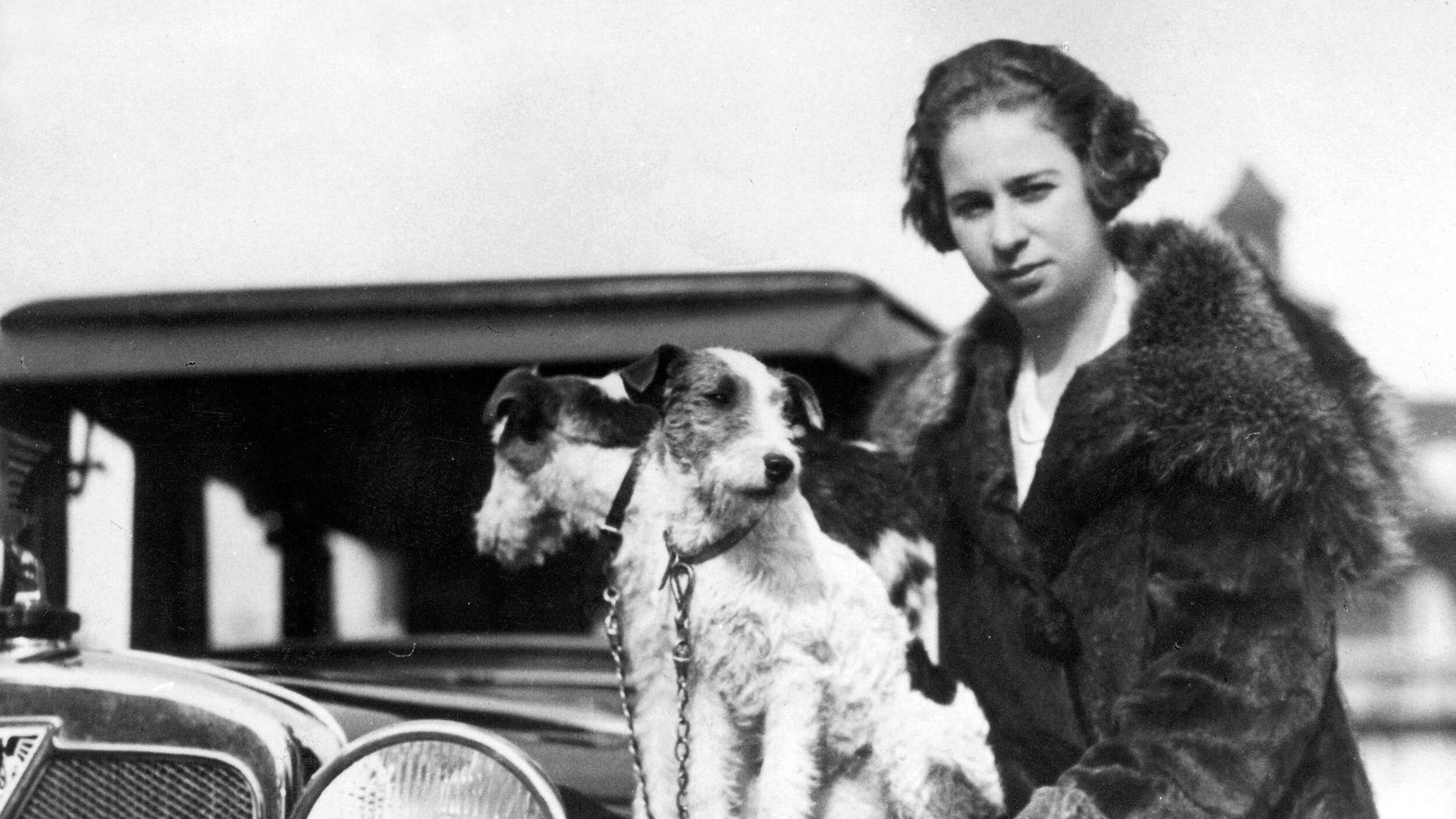 Historische schwarz-weiß Aufnahme zeigt die Rennfahrerin Clärenore Söderström-Stinnes im Jahr 1927 vor einem Automobil. 
