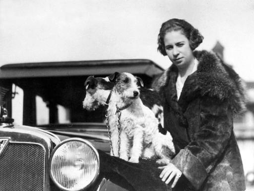 Historische schwarz-weiß Aufnahme zeigt die Rennfahrerin Clärenore Söderström-Stinnes im Jahr 1927 vor einem Automobil. 
