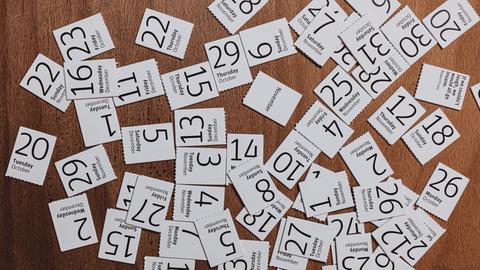 Blick auf eine Schreibtischplatte aus Holz, auf dem viele abgerissene Kalenderblätter liegen.