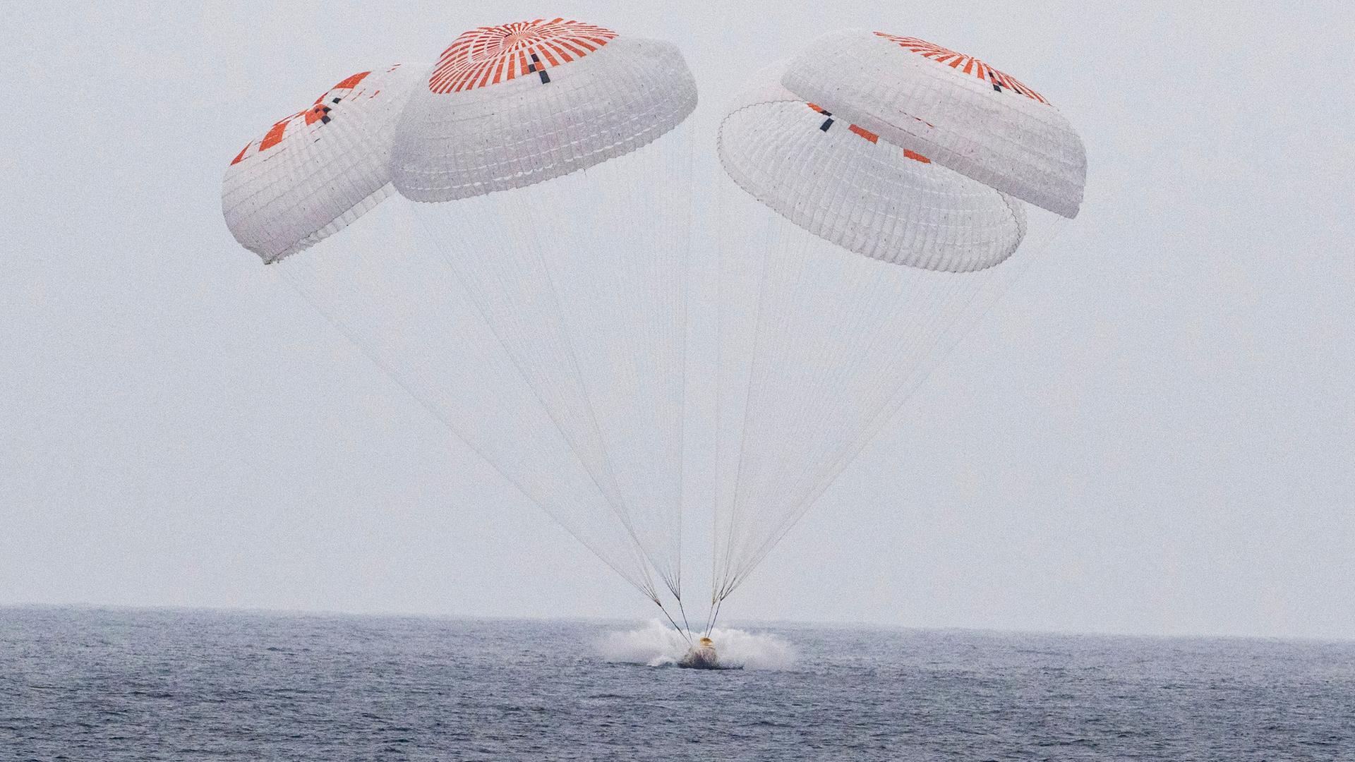 Die die SpaceX-Kapsel landet an Fallschirmen auf dem Meer. Die die SpaceX-Kapsel landet an Fallschirmen auf dem Meer.
