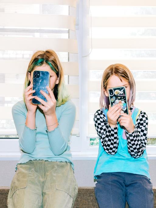Zwei Kindernutzen jeweils ein Smartphone und verdecken damit ihre Gesichter. 