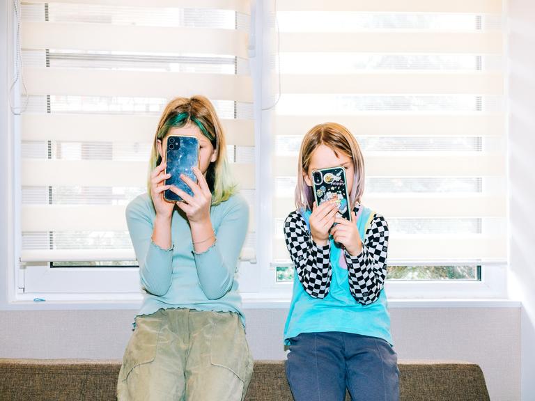 Zwei Kindernutzen jeweils ein Smartphone und verdecken damit ihre Gesichter. 